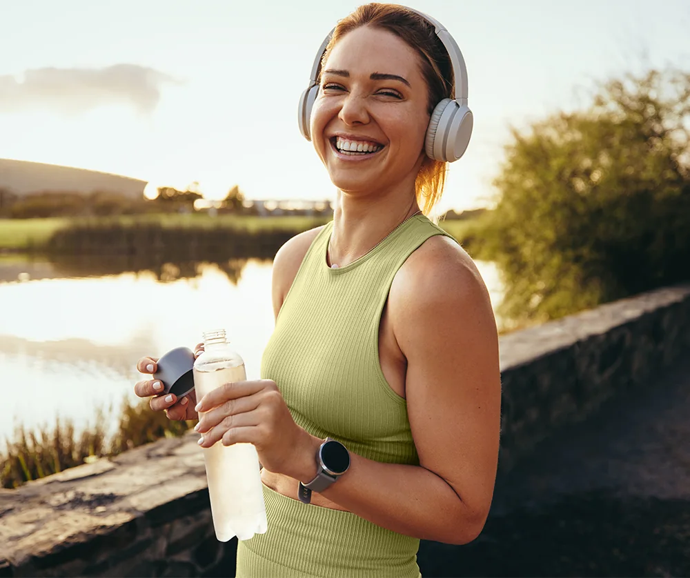 happy young woman taking drink of water during evening jog