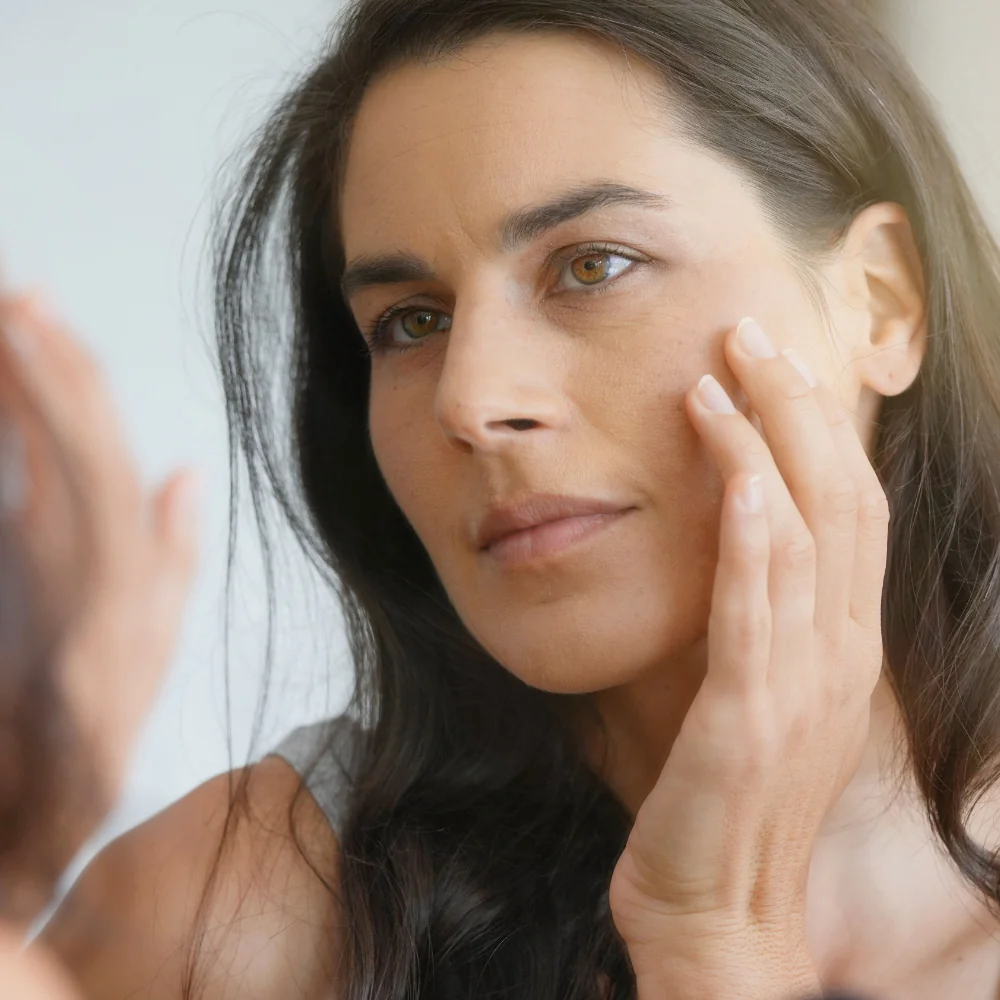 middle-aged woman looking in mirror touching skin